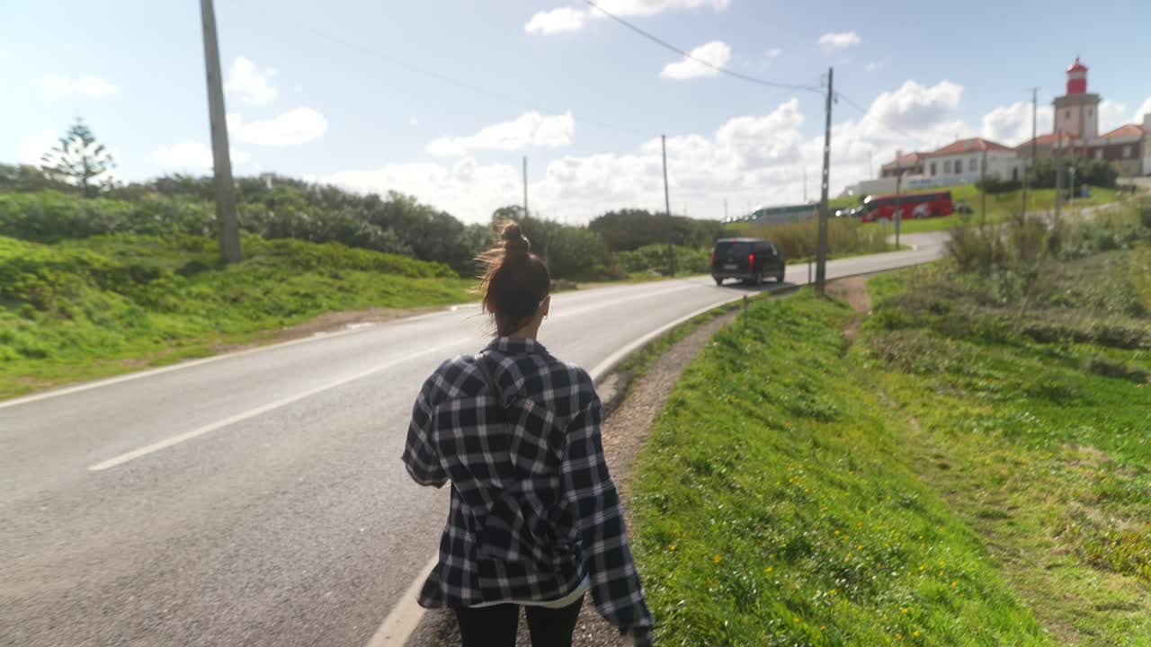 Woman walking on a coastal road near a lighthouse