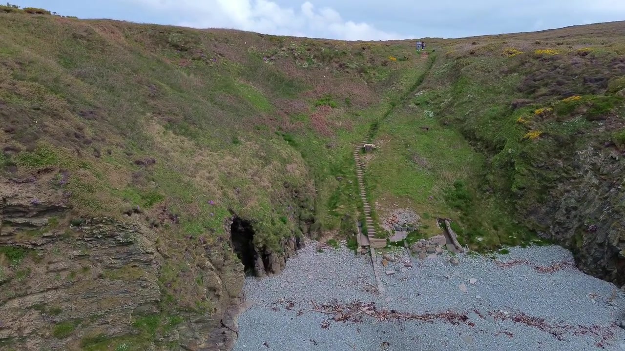 Slowly flying between rugged welsh formation rising to green moorland headland hillside