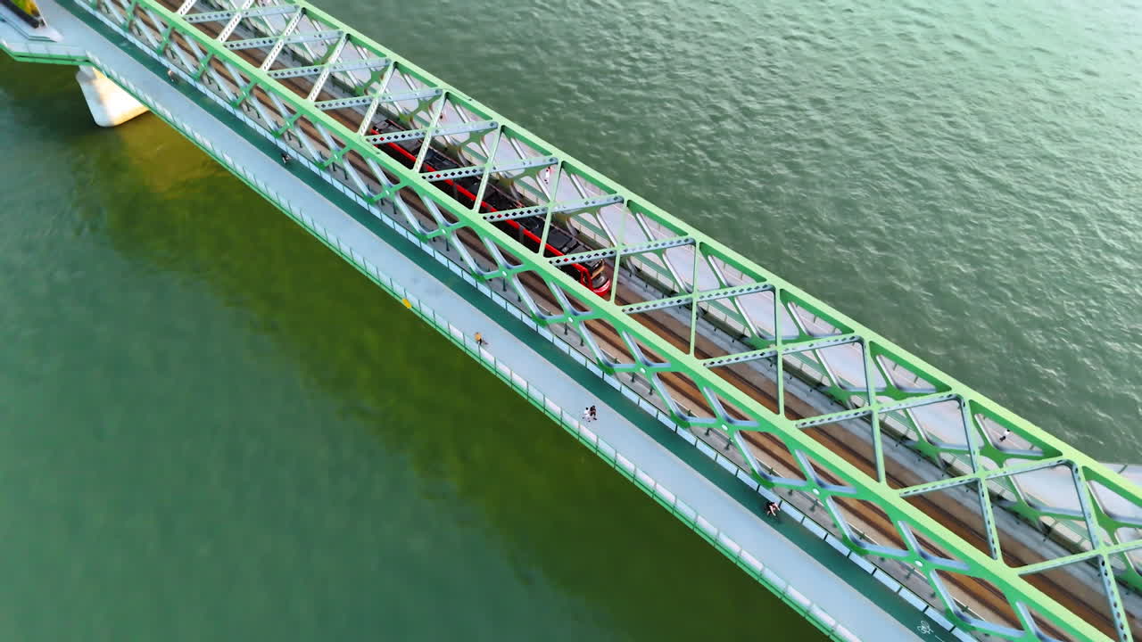 Following a tram moving by the Old Bridge crossing the Danube. Some people walk by the pedestrian part of the construction. Top view. Bratislava, Slovakia