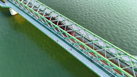 following a tram moving by the old bridge crossing the danube. some people walk by the pedestrian part of the construction. top view. bratislava, slovakia