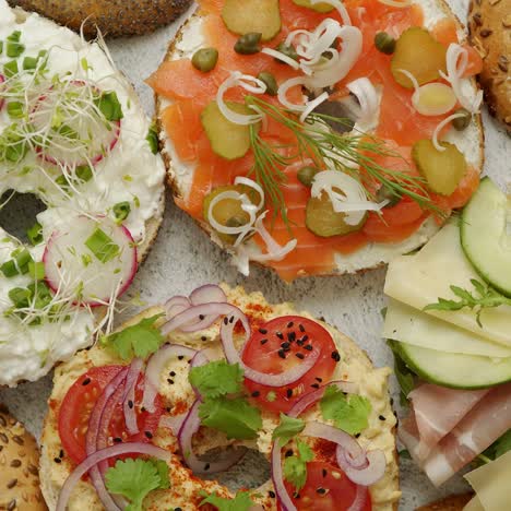 bagel sandwiches with various toppings  salmon  cottage cheese  hummus  ham  radish and fresh herbs