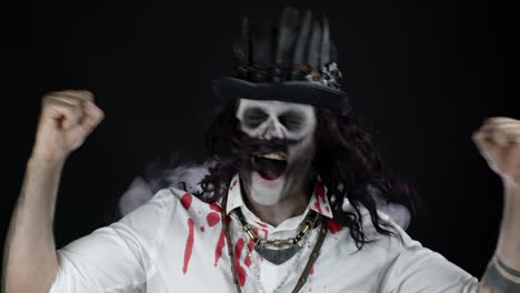 hombre siniestro con maquillaje de esqueleto de halloween en camisa con sangre celebrando, mostrando los pulgares hacia arriba