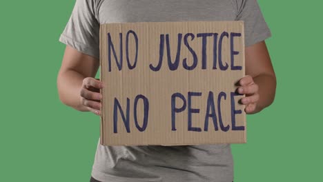 man holds in front of him a poster from a cardboard box with the words no justice no peace. concept of strike and anti racism. isolated a green screen, chroma key. close up. slow motion