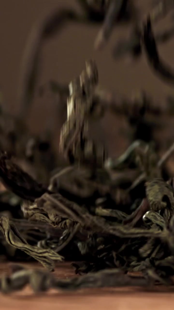 Dried Green Tea Leaves Falling onto a Wooden Surface in Slow Motion