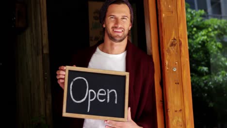 smiling owner leaning at door with open sign board in cafe