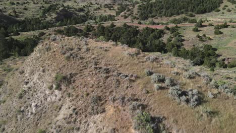 fly by view of a large hill with a meadow on top and off road trails beyond in wyoming on a summer day