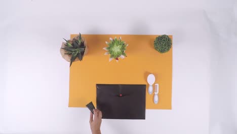 top down view of beauty salon utensils placed on orange paper on white background with small plants and black envelope