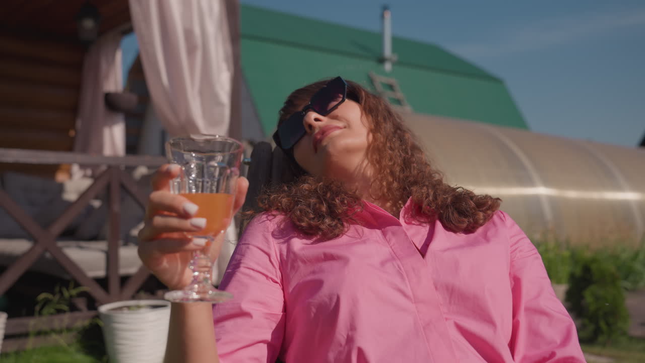 Elegant Woman Savoring Lime Beverage Outside, Woman In Bright Attire Relaxing In Peaceful Backyard Setting, Lady With Sunglasses Parks On Patio Sipping Juice And Embracing Tranquil Morning
