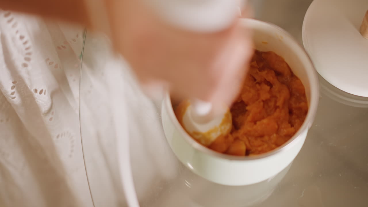 Caucasian hands blending pumpkin puree in bowl, closeup topdown shot of immersion blender whipping smooth orange filling on linen, warm natural light, gentle homely pace, baker preparing pie filling