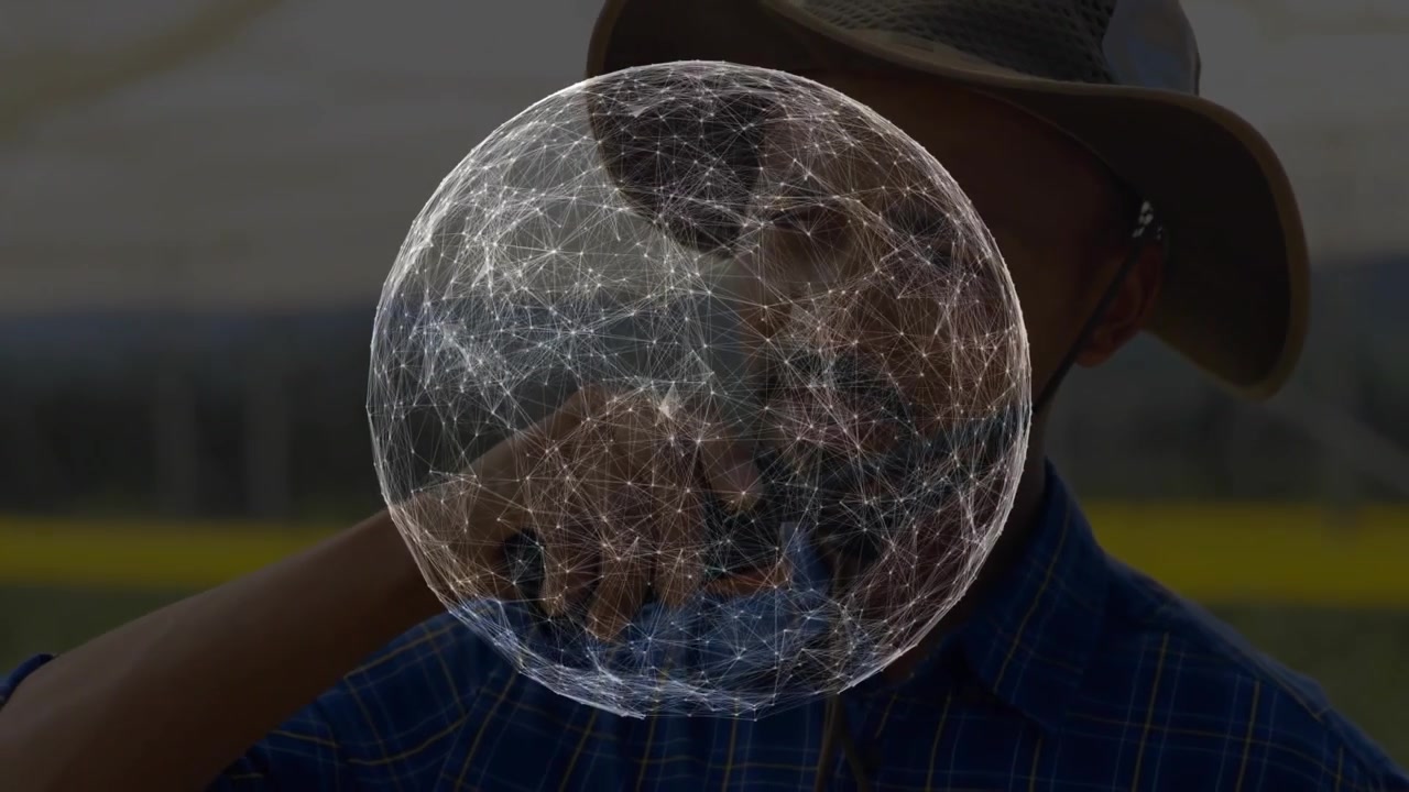 Uomo in piedi in un campo erboso con una sfera tecnologica digitale che rimane al centro dell'inquadratura e si aggiusta la tesa del cappello.