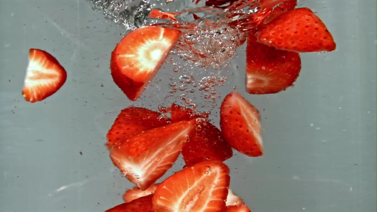 Fragole rosse fresche e metà che cadono in acqua limpida al rallentatore