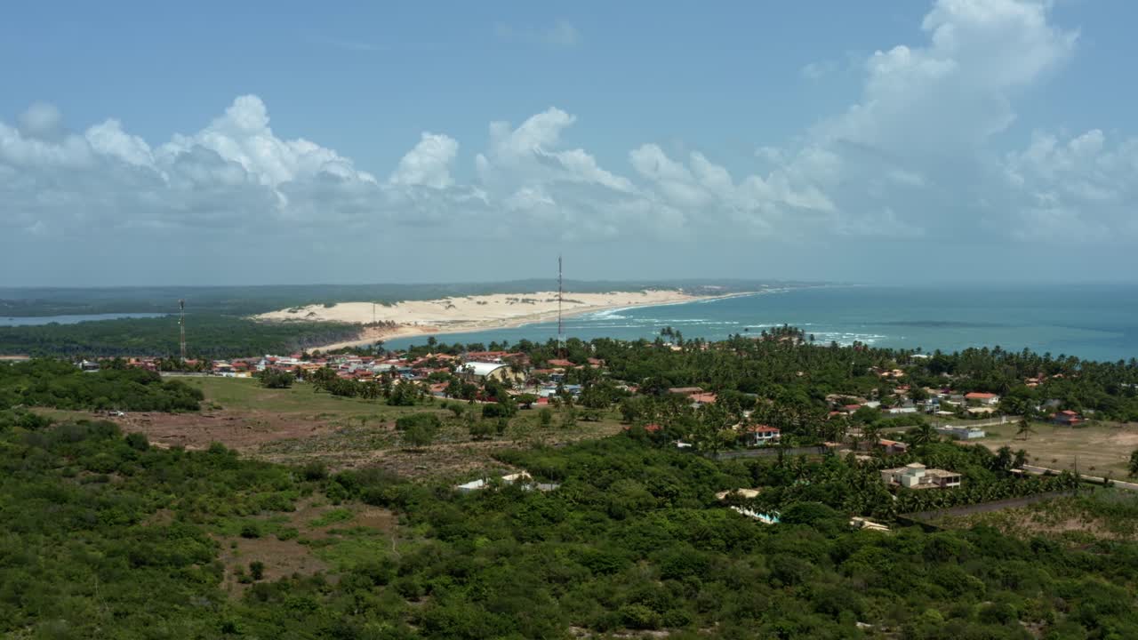 Right trucking aerial drone wide shot of the tropical beach town of Tibau do Sul in Rio Grande do Norte, Brazil with the Malemb&aacute; Sand Dunes, Atlantic Ocean, and Guara&iacute;ras Lagoon in the background