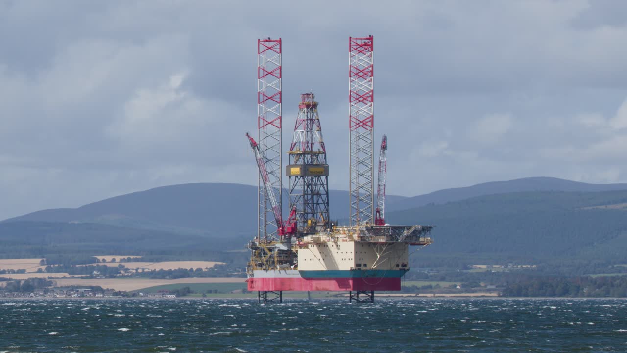 Stationary offshore oil rig in windy sea, distant hills, daylight, wide shot, slight camera shake