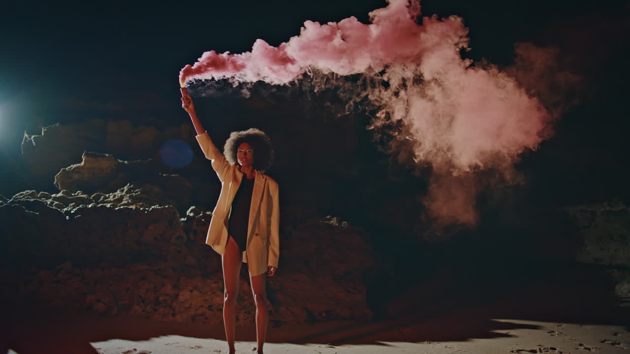 Woman celebrating smoke bomb on night performance. Sexy girl standing dark beach