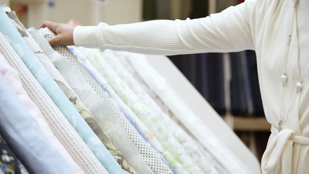 una hermosa chica compradora en una tienda de telas. ella elige un rollo de tela con puntos polka entre la gama de telas ligeras. cámara lenta