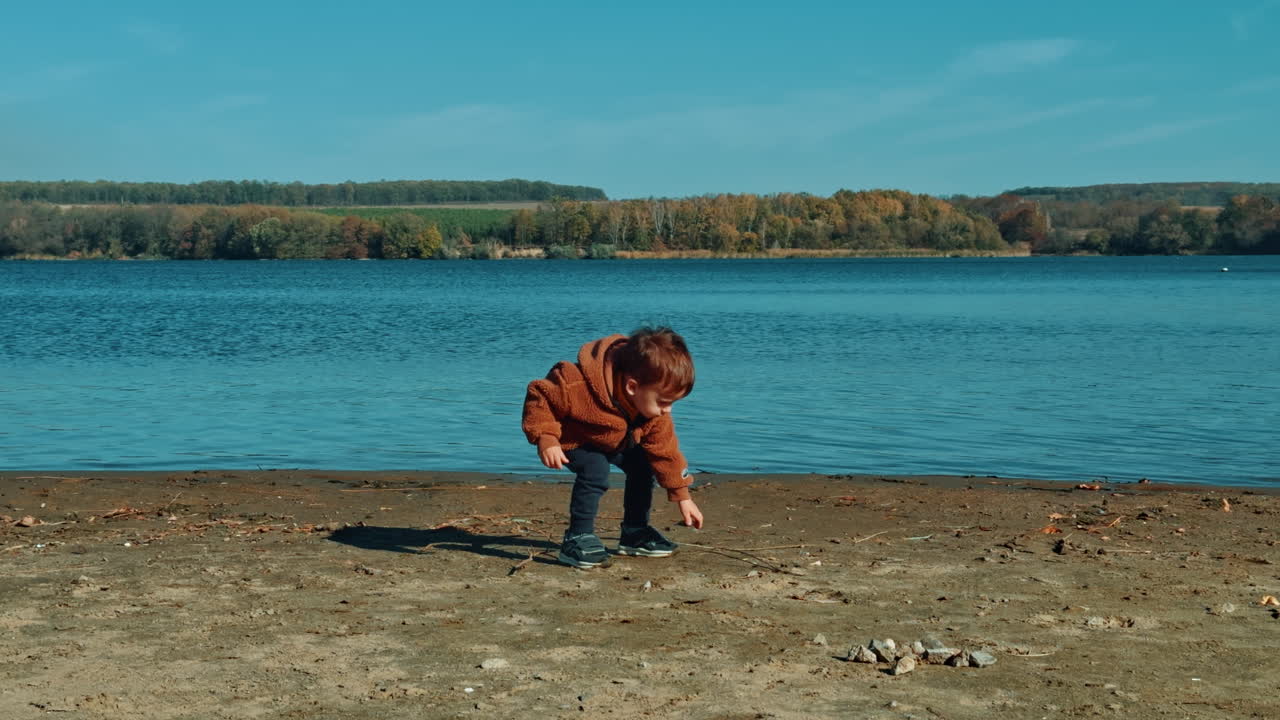 Baby boy spending time on the river bank. Child goes to the water and throws a stone happily.