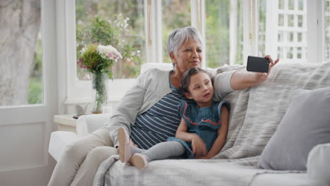 Kleines-Mädchen-Nutzt-Smartphone-Mit-Großmutter-Beim-Videochat,-Winkt-Der-Familie-Zu-Und-Teilt-Ihr-Urlaubswochenende-Mit-Oma,-Die-Auf-Dem-Handy-Chattet-Und-Sich-Zu-Hause-Mit-Enkelin-In-4k-Entspannt