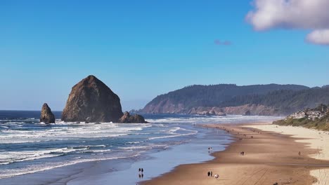 tourists strolling on cannon beach with haystack rock at the shoreline in clatsop county, oregon