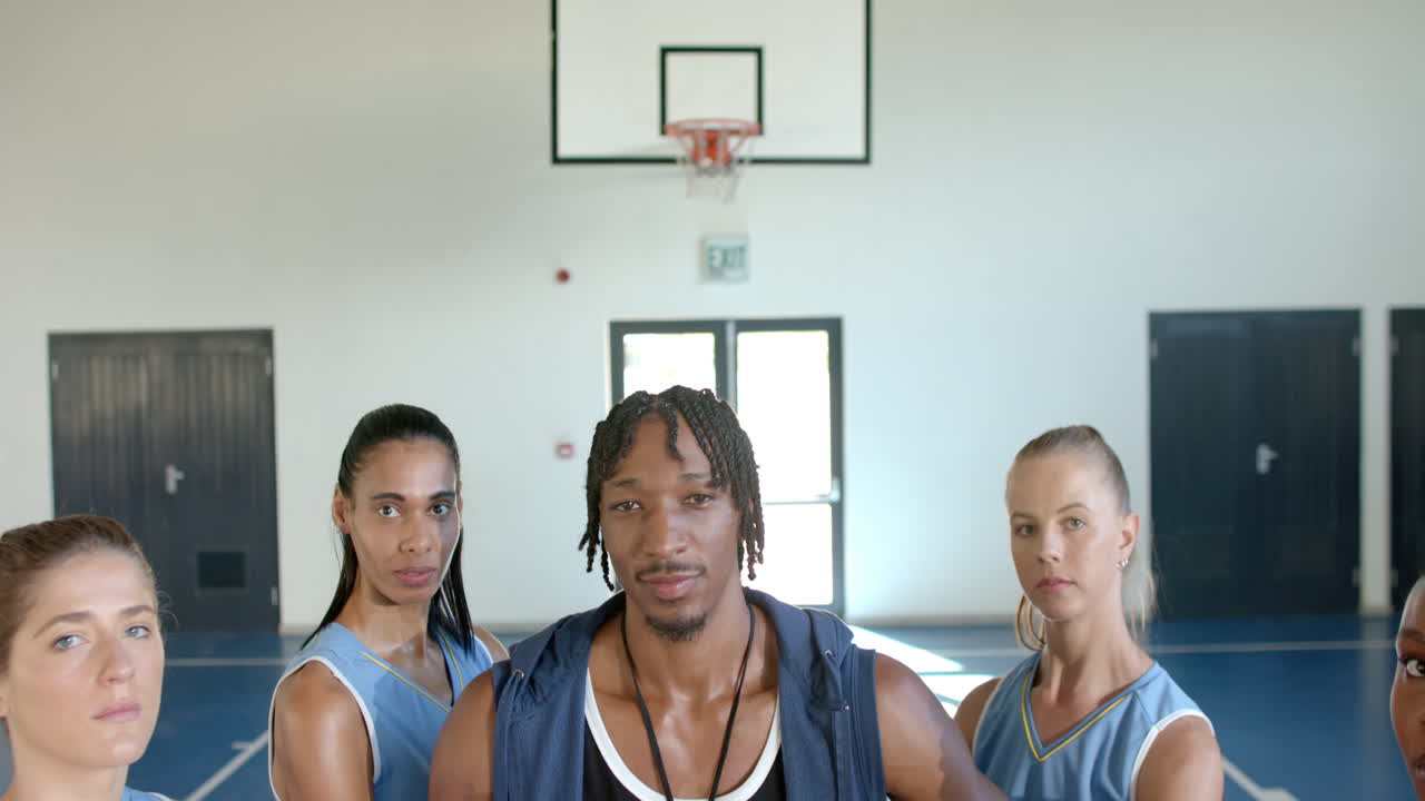 Basketballtrainer steht mit weiblichen Teamspielerinnen in der Turnhalle und wirkt selbstbewusst.