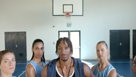 basketball coach standing with female team players in gym, looking confident
