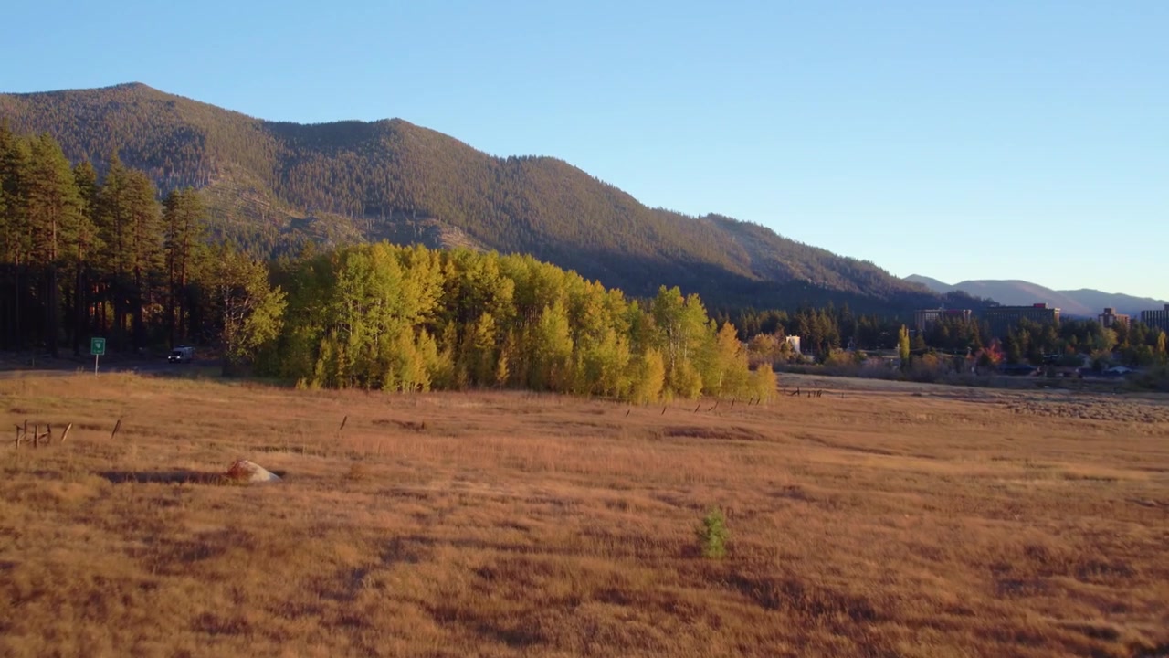 Ripresa aerea dinamica che mostra un sereno paesaggio alpino con colori autunnali, terreno aperto e uno sfondo montuoso sotto cieli sereni