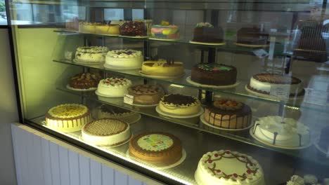 various cakes and birthday cakes on a glass counter in a pasta shop at daytime in 4k