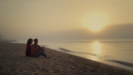 couple sitting on beach at sunset. woman and man enjoying ocean landscape