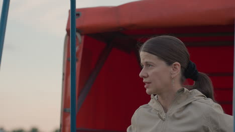 woman instructing crew during setup of hot air balloon basket near trailer holding rope against red cover background expressing focus and teamwork under cloudy sky