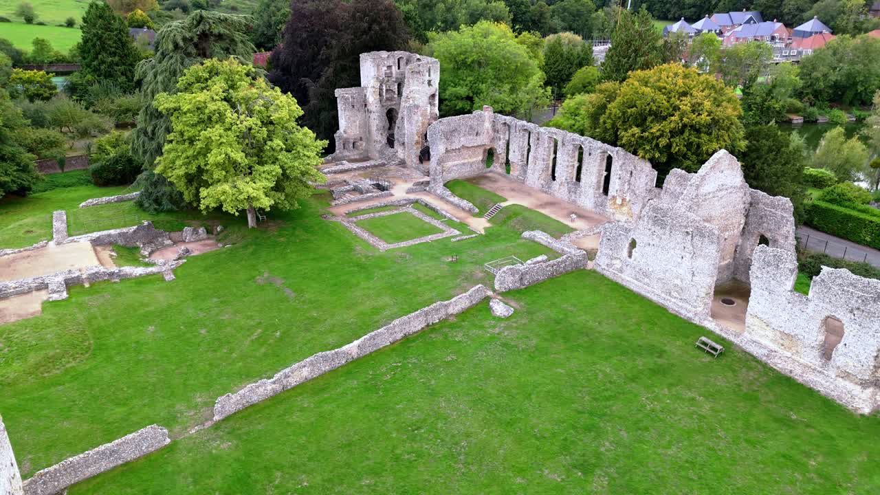 Low-angle aerial drone pans right over Bishop’s Waltham Palace ruins in town, showcasing historic stone walls, autumn trees, and golden sunset light casting warm tones across the village