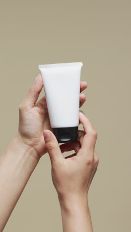 hands of woman holding tube of cream on beige background with copy space, slow motion