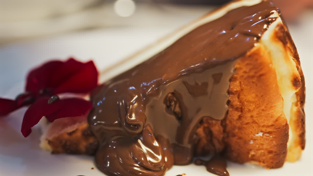 Close up of chocolate pouring on a slice of cheesecake on a white plate