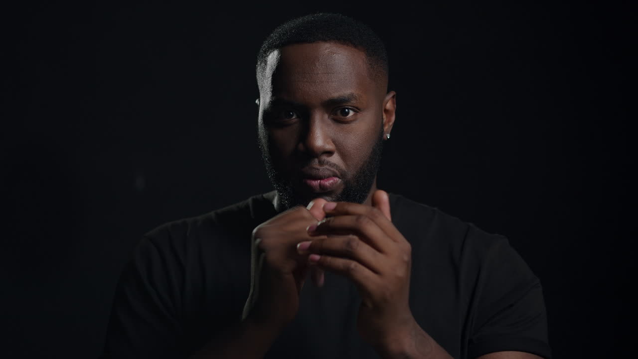 Anxious man warming up hands on black background. Afro guy screaming indoors