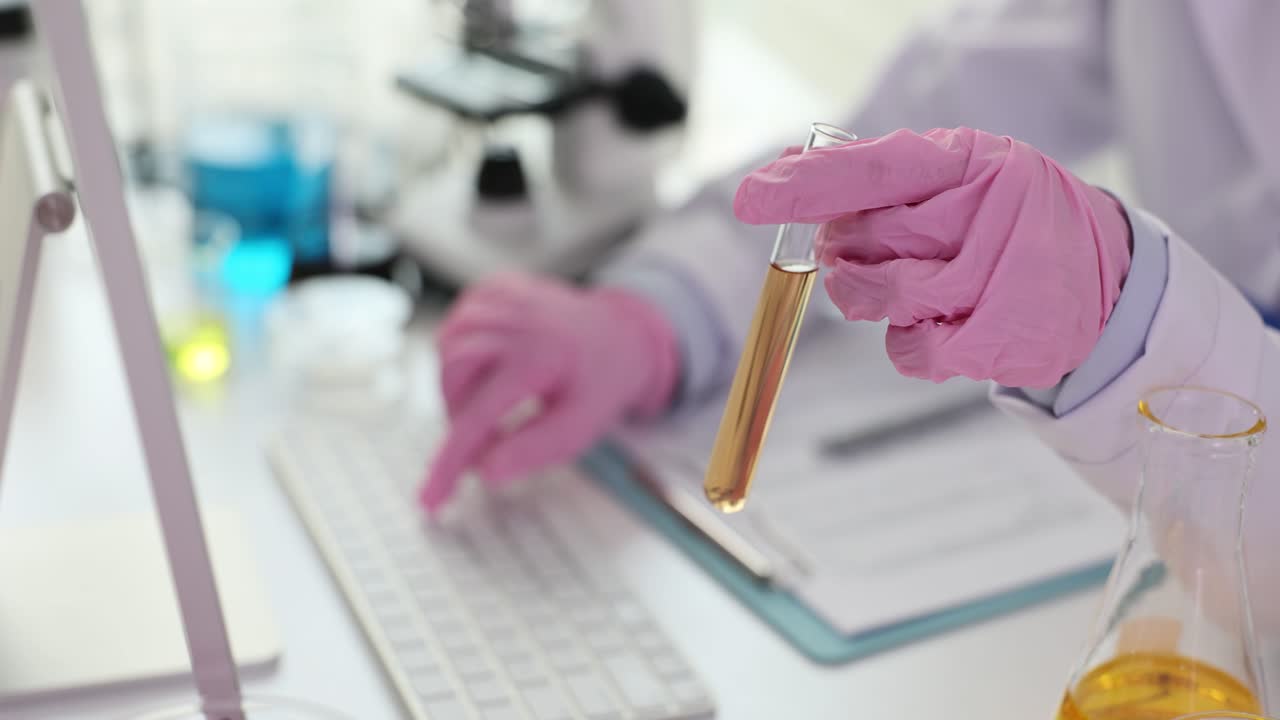 Scienziato in camice da laboratorio e guanti rosa che tiene una provetta in un laboratorio
