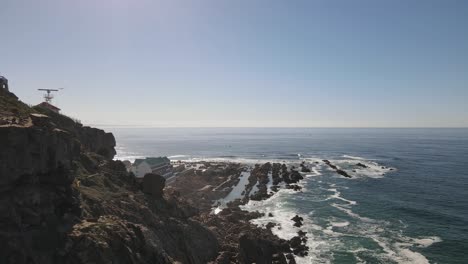 Drone-shot-flying-on-the-edge-of-a-rocky-cliff-over-a-small-ocean-town-on-a-summers-day