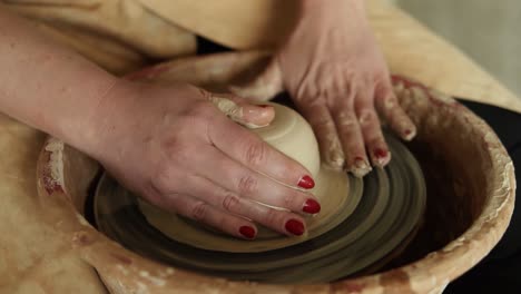 Primer-Plano-De-Las-Manos-De-Alfarero-Con-Manicura-Roja-Trabajando-Con-Arcilla-Húmeda-En-Una-Rueda-De-Alfarería-Haciendo-Un-Producto-De-Arcilla-En-Un-Taller-1