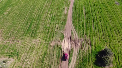 Bird's-eye-view-aerial-shot-of-a-red-car-as-it-splashes-through-a-puddle-on-a-country-road-in-scenic-Akamas-Peninsula,-Cyprus