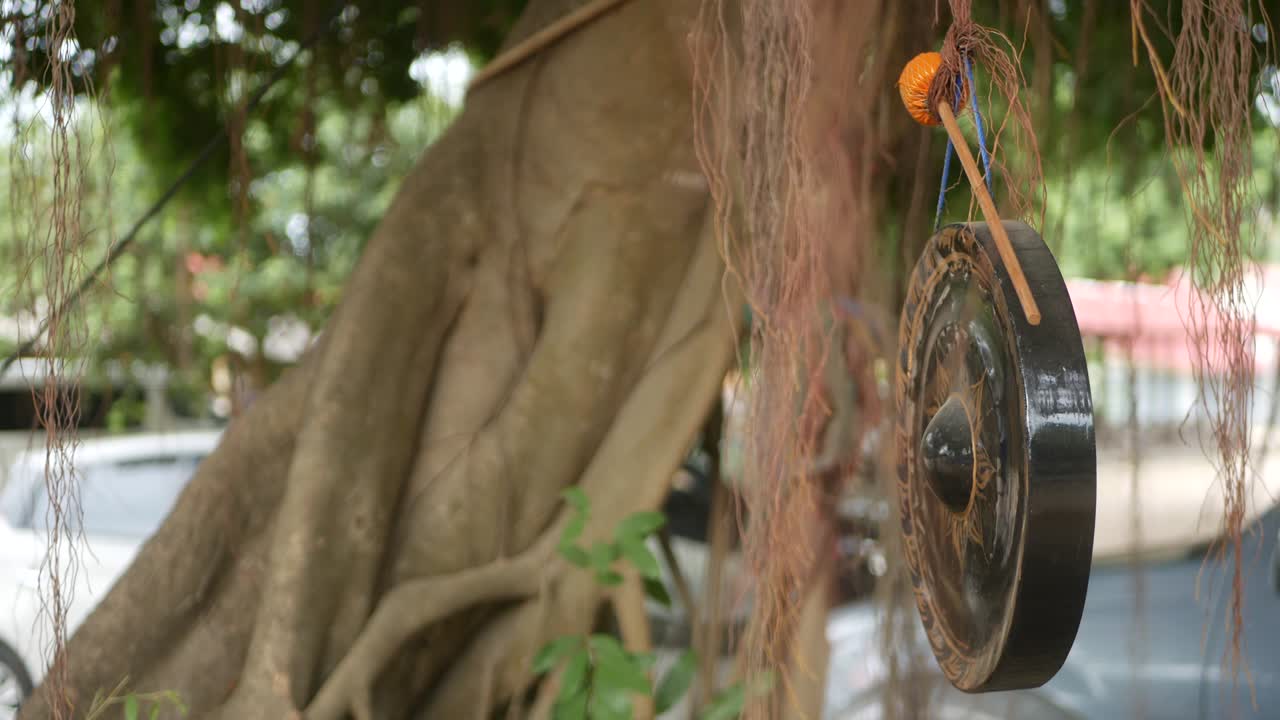 Small traditional gong hanging on background of old banyan tree in daylight. Symbol of buddhist religion. Tropical idyllic natural background. Zen meditation, retreat and enlightenment concept.