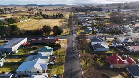 aerial footage captures a quiet residential street in a small australian town, with houses, trees, and morning sunlight. smooth forward drone movement reveals urban layout