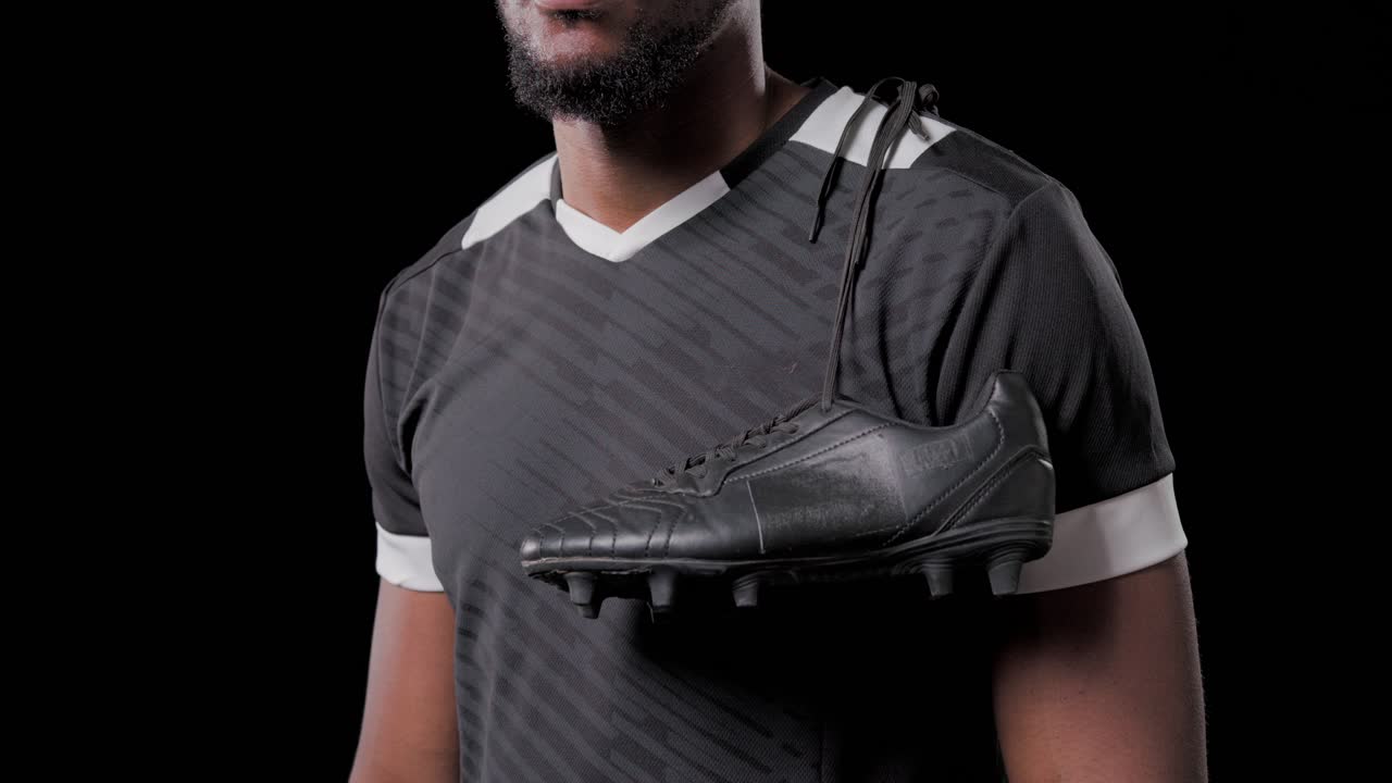 Plano de cámara alejándose de un hombre afroamericano posando con un uniforme, con un taco de zapato deportivo colgando sobre el hombro derecho para un anuncio.