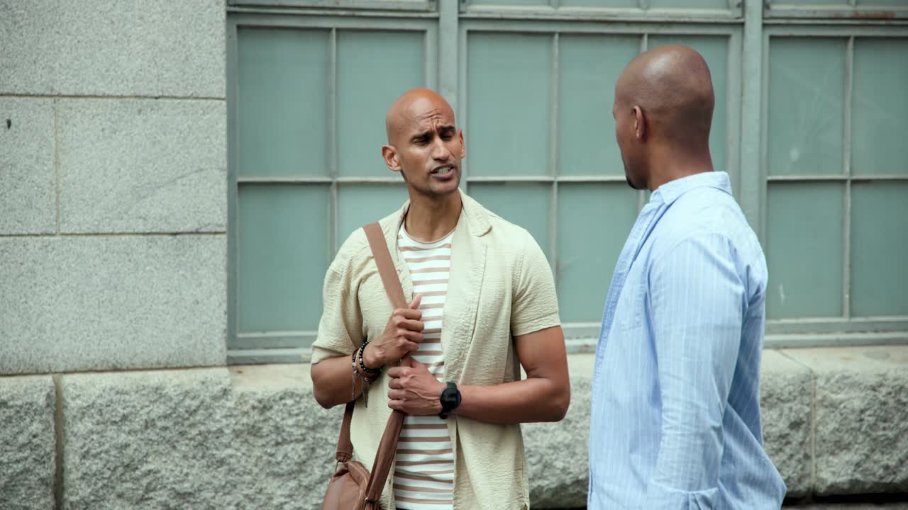Diverse men exchanging looks, speaking and gesturing on sidewalk with bag and phone, catching up