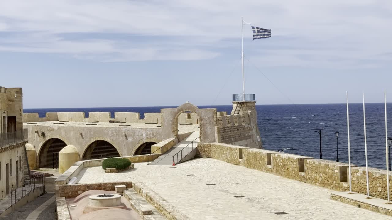 B-roll di viaggio cinematografico della Fortezza di San Salvador a Chania, Creta, con la bandiera greca che sventola sopra storiche mura veneziane che si affacciano sul Mar Mediterraneo e senza persone.