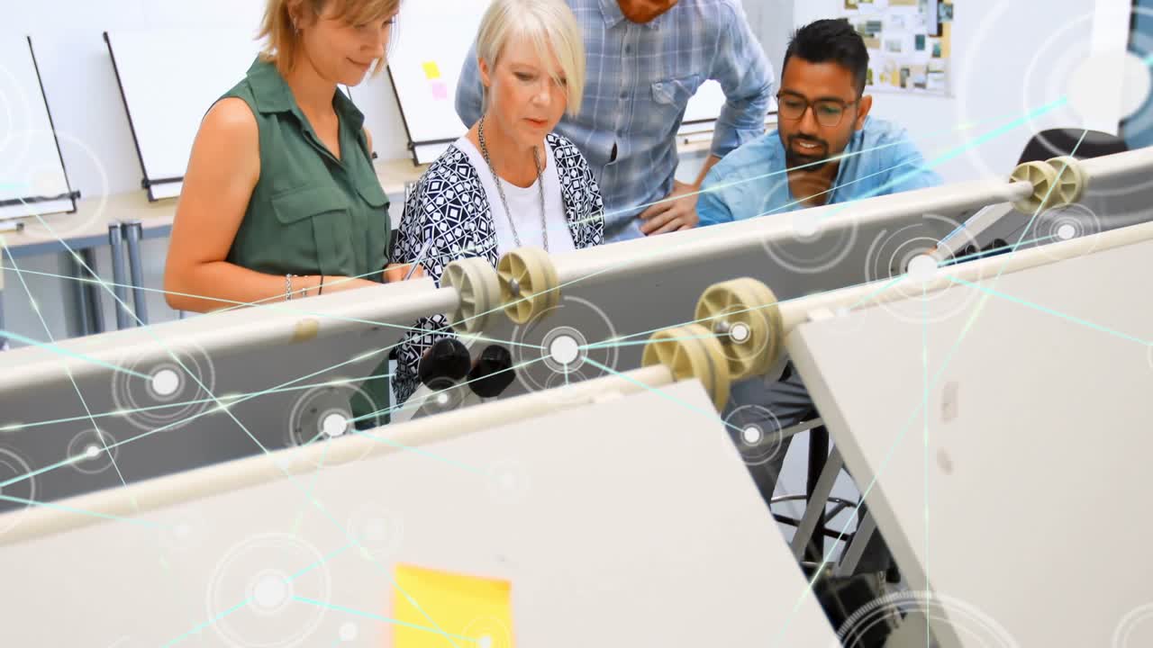 Design team examining pulley model in design studio, displaying digital node network overlay