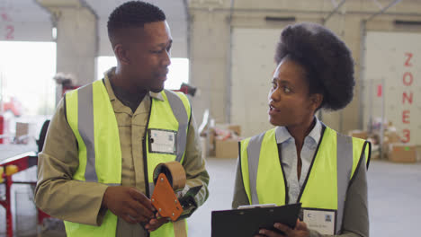 african american male and female workers with clipboard talking in warehouse
