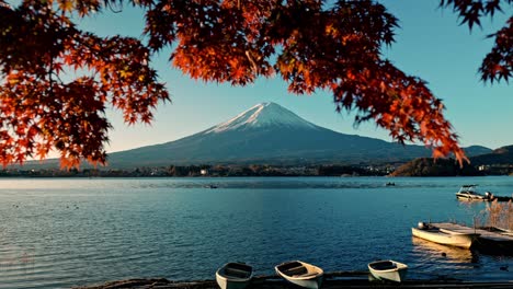 the serene shore of lake kawaguchiko is dotted with small boats, framed by vibrant red autumn foliage.