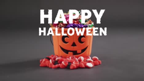 Animation-of-halloween-text-over-carved-pumpkin-bucket-with-sweets-on-grey-background