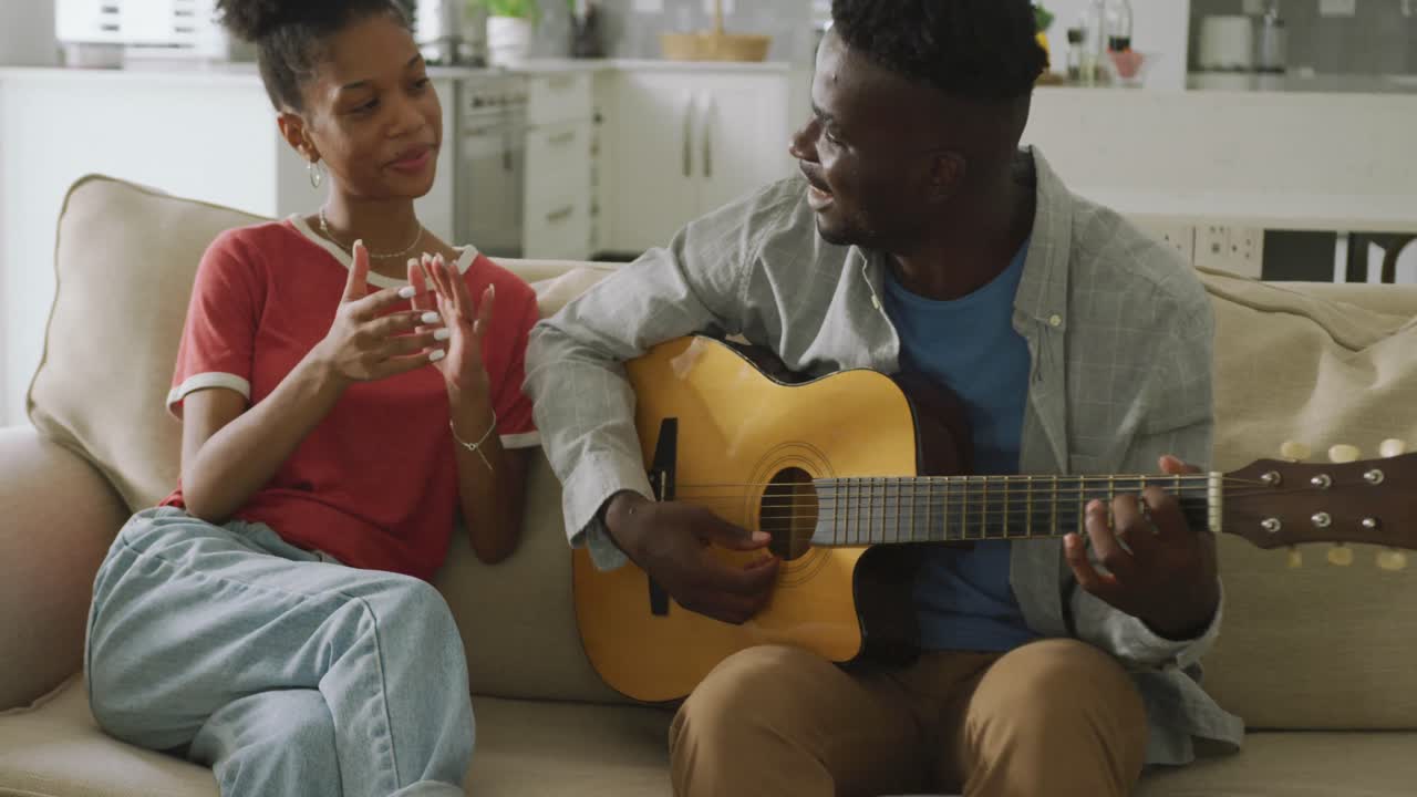 Video di una coppia afroamericana felice seduta sul divano, che canta e suona la chitarra