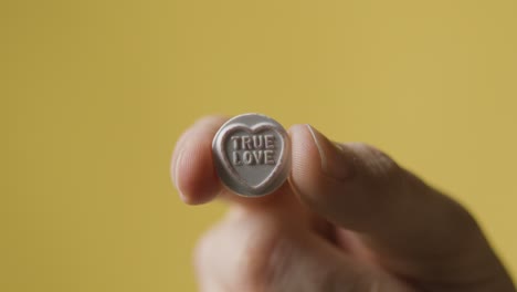 close up of hand holding heart candy avec true love message sur fond jaune