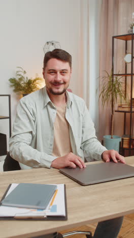smiling caucasian young man freelancer closing laptop after work sitting at home office table