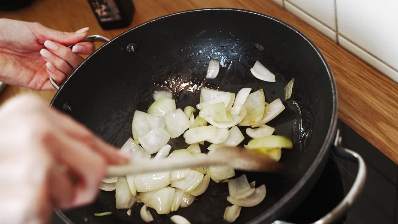 Woman's hands stirfrying onion on a frypan in slow motion