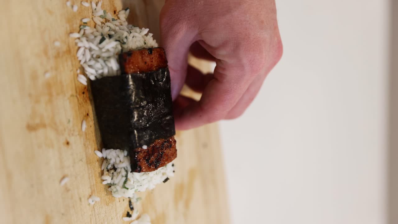 envolviendo el arroz hawaiano spam musubi con algas marinas, verticalmente